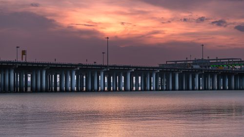 Free A stunning view of a bridge during sunset with vibrant clouds and calm water reflection. Stock Photo