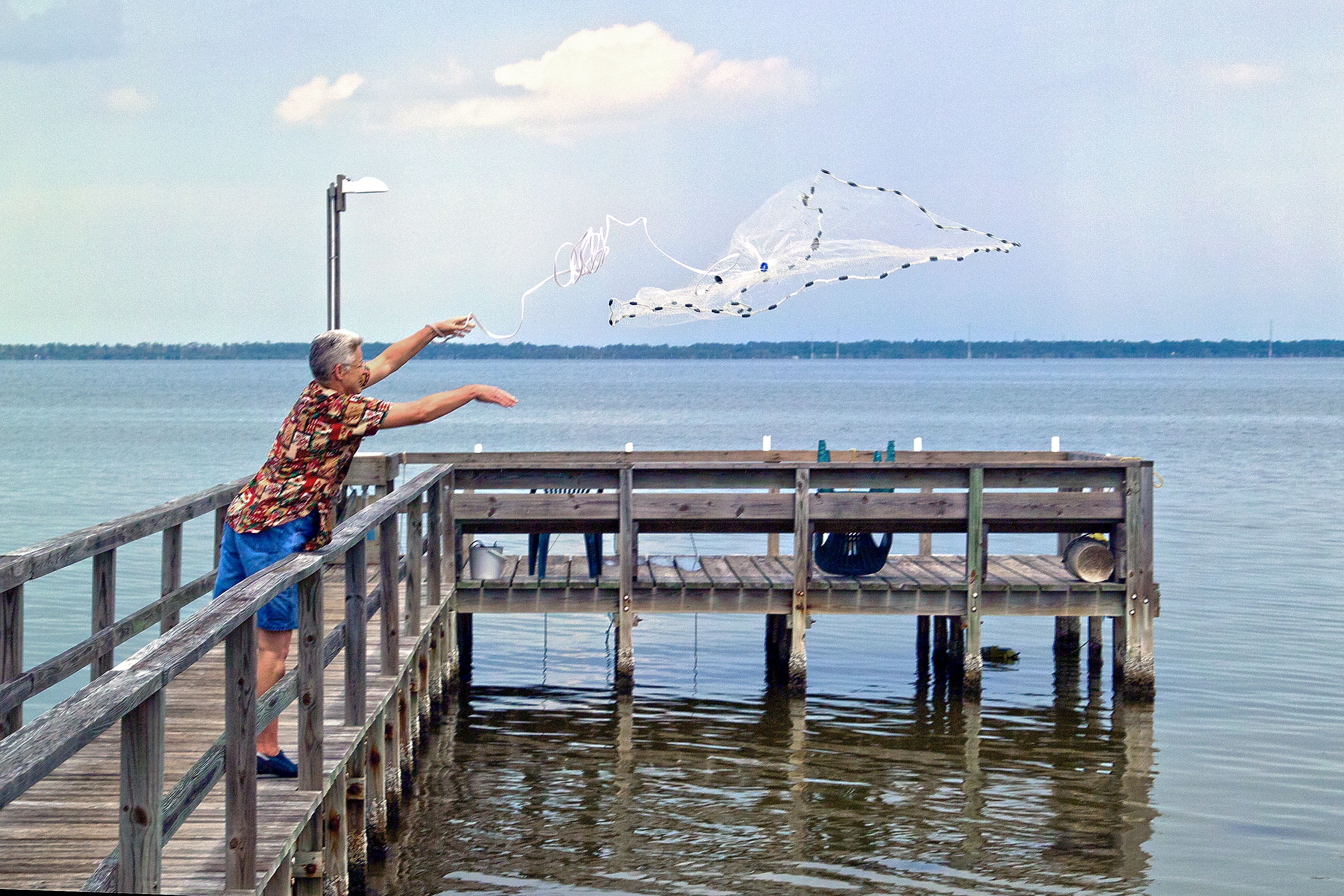 A man casting a net from a dock into a serene lake in Florida, showcasing traditional fishing techniques.