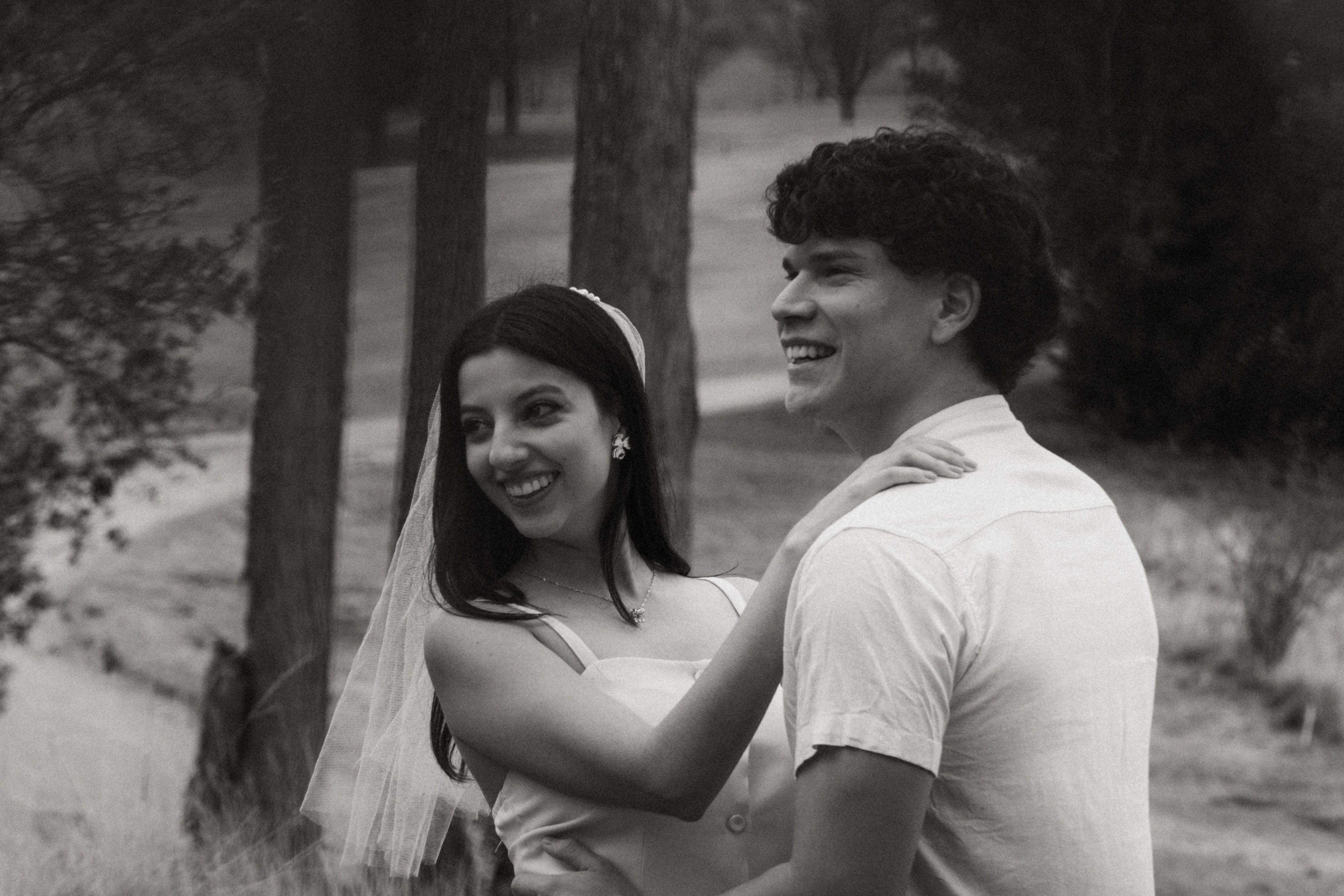 Smiling couple embracing outdoors in black and white image, capturing a joyful moment.