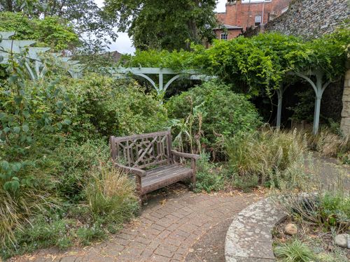 Free Cozy garden with a wooden bench surrounded by vibrant greenery, perfect for relaxation. Stock Photo