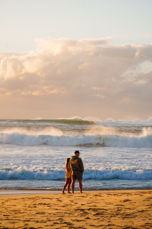 Free A couple walks along the beach at sunset, enjoying the waves and the warm light. Stock Photo