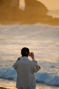 A person photographing a serene ocean sunset on the beach with a smartphone.
