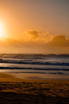Golden sunrise over ocean waves with a calm beach foreground.