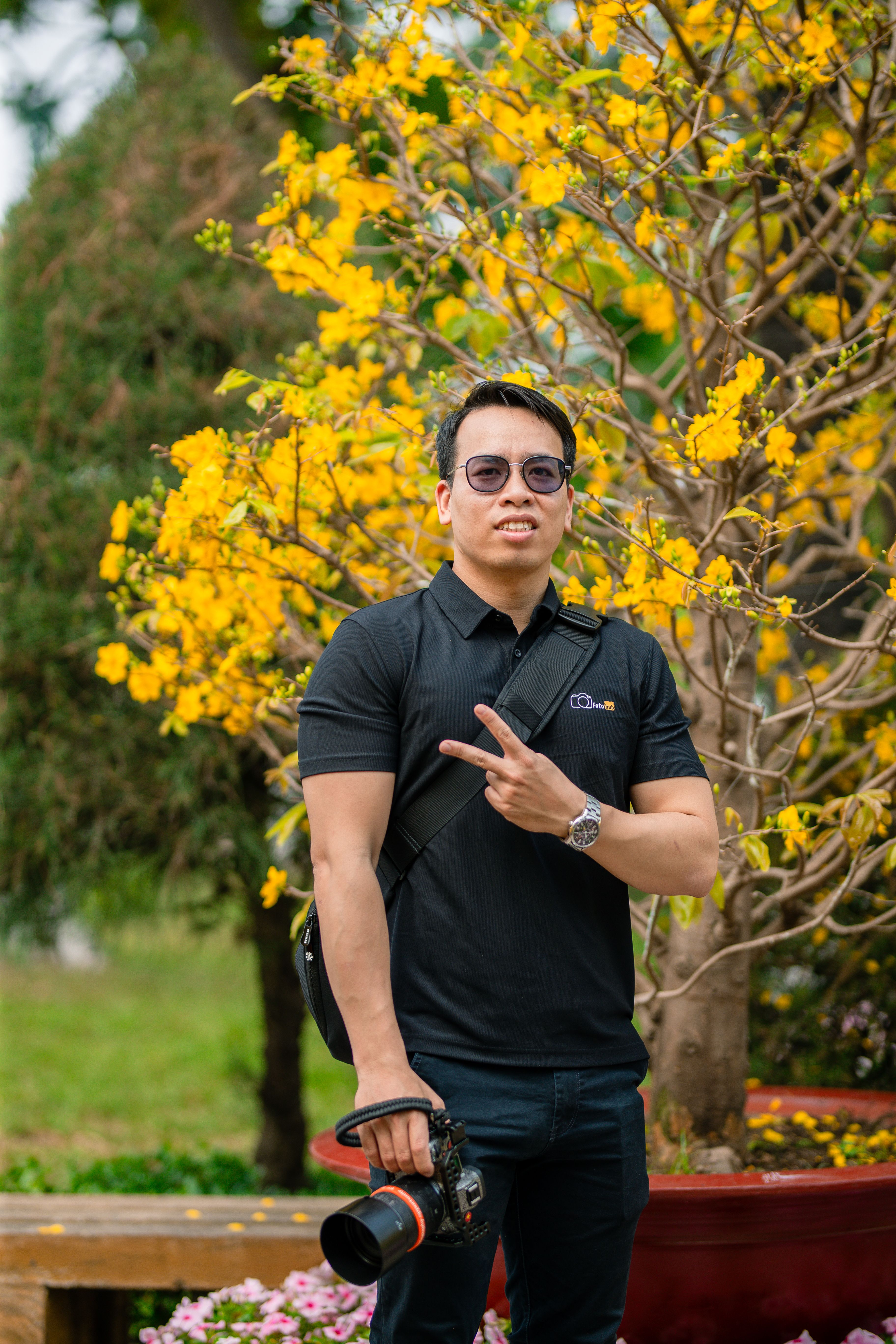Photographer posing with camera near vibrant yellow blossoms outdoors.