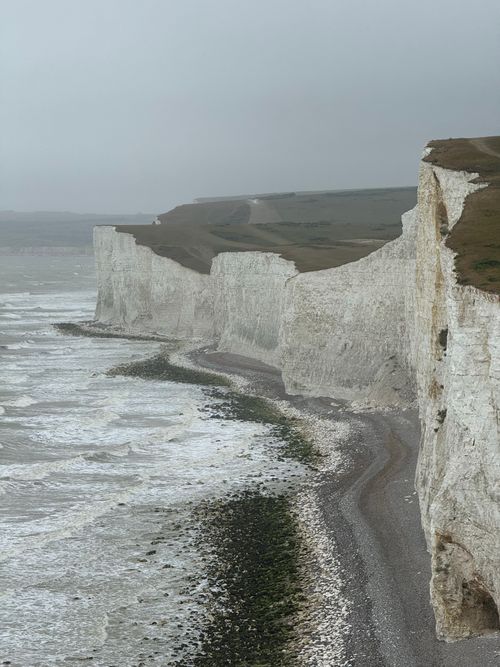 Free Majestic White Cliffs of Dover with cloudy skies and ocean waves crashing below. Stock Photo