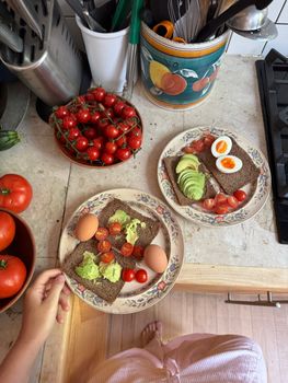 Rye bread with avocado, cherry tomatoes, and boiled eggs on a kitchen counter.