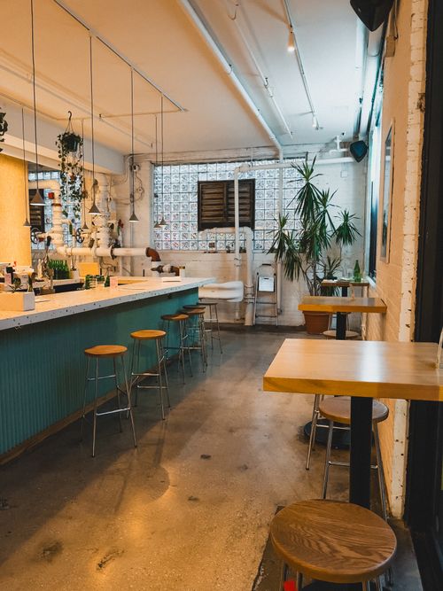 Free Warm and inviting modern café interior featuring a stylish bar, seating, and lush plants. Stock Photo