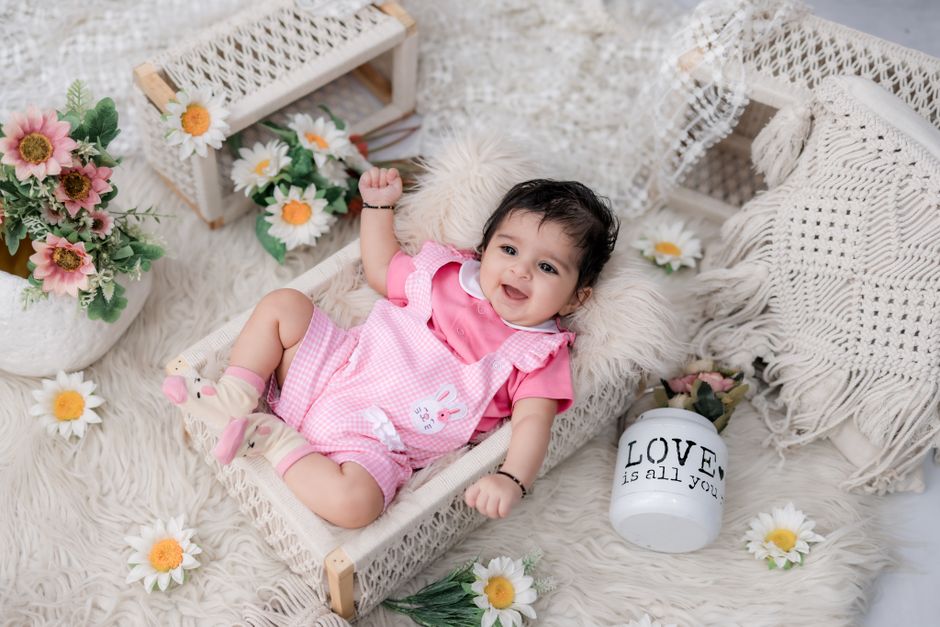 Adorable baby lying on fluffy rug surrounded by flowers in a cozy indoor setup.