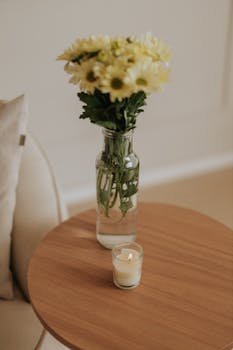 A minimalist interior featuring a vase of yellow flowers and a lit candle on a wooden table.