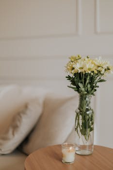 Elegant minimalist decor featuring flowers in a vase and a lit candle on a wooden table.