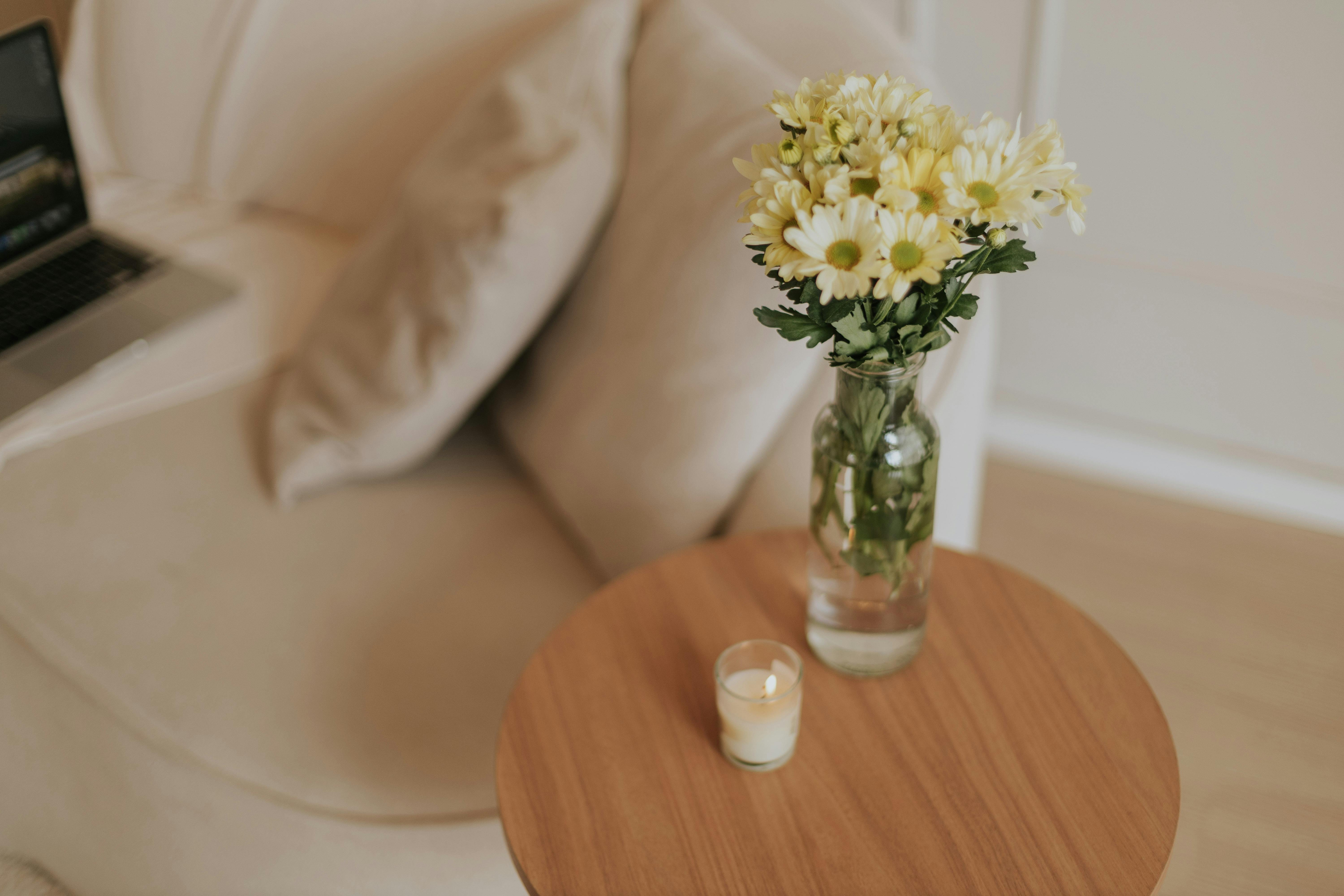 Elegant home interior showcasing a minimalist setting with daisies and a warm candle on a wooden table.