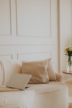A serene and stylish home office with a neutral aesthetic featuring a laptop and cozy seating.