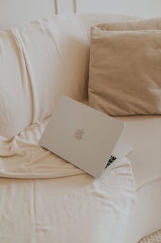Minimalist home office setup with a laptop on a soft beige sofa, perfect for remote work inspiration.
