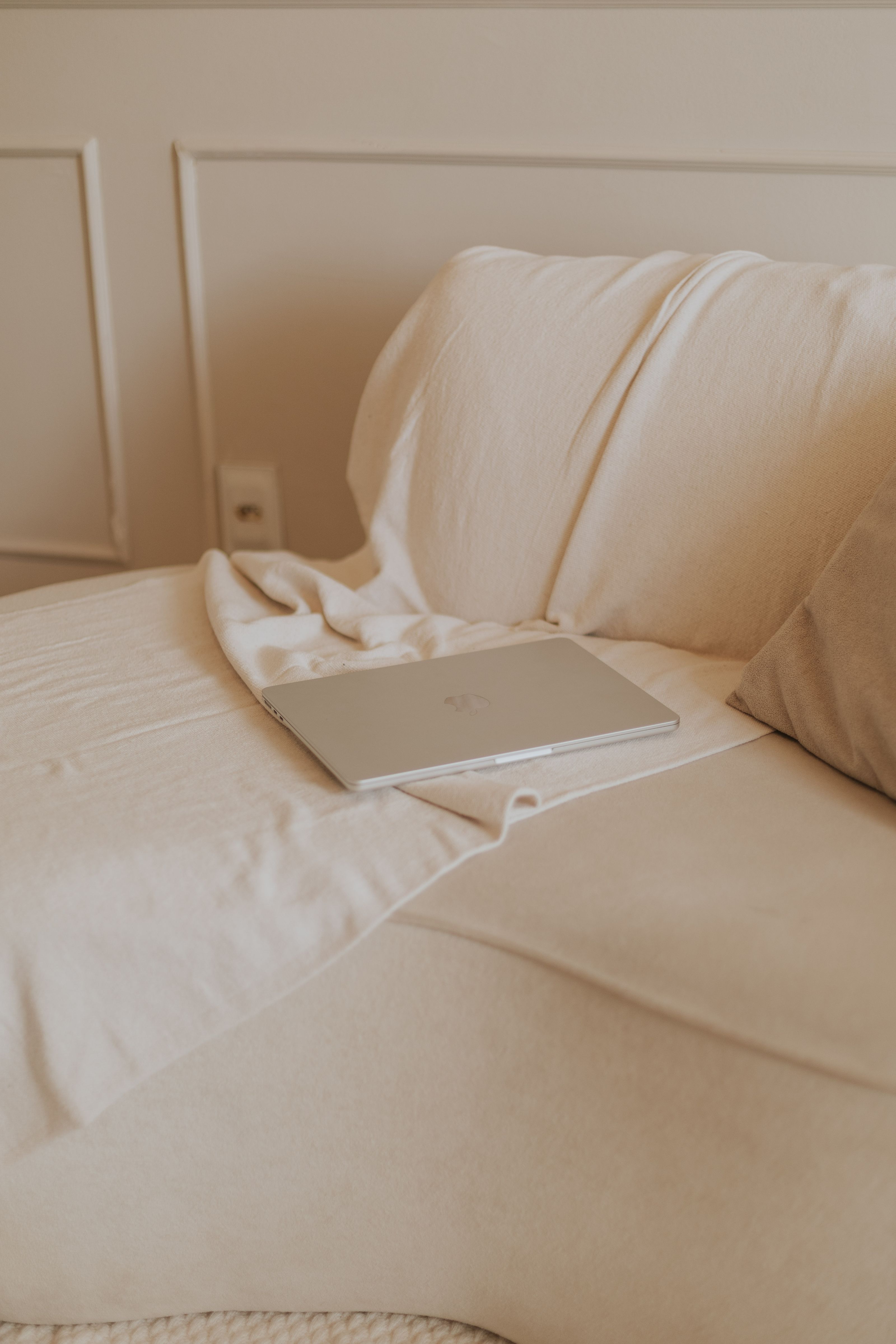 Uma configuração de escritório em casa serena com um laptop fechado em um sofá bege, transmitindo uma vibe minimalista e pacífica.