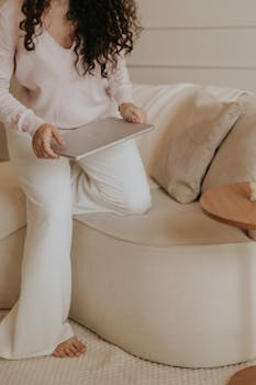 A serene home workspace featuring a woman with a laptop, soft neutral tones, and minimalist decor.