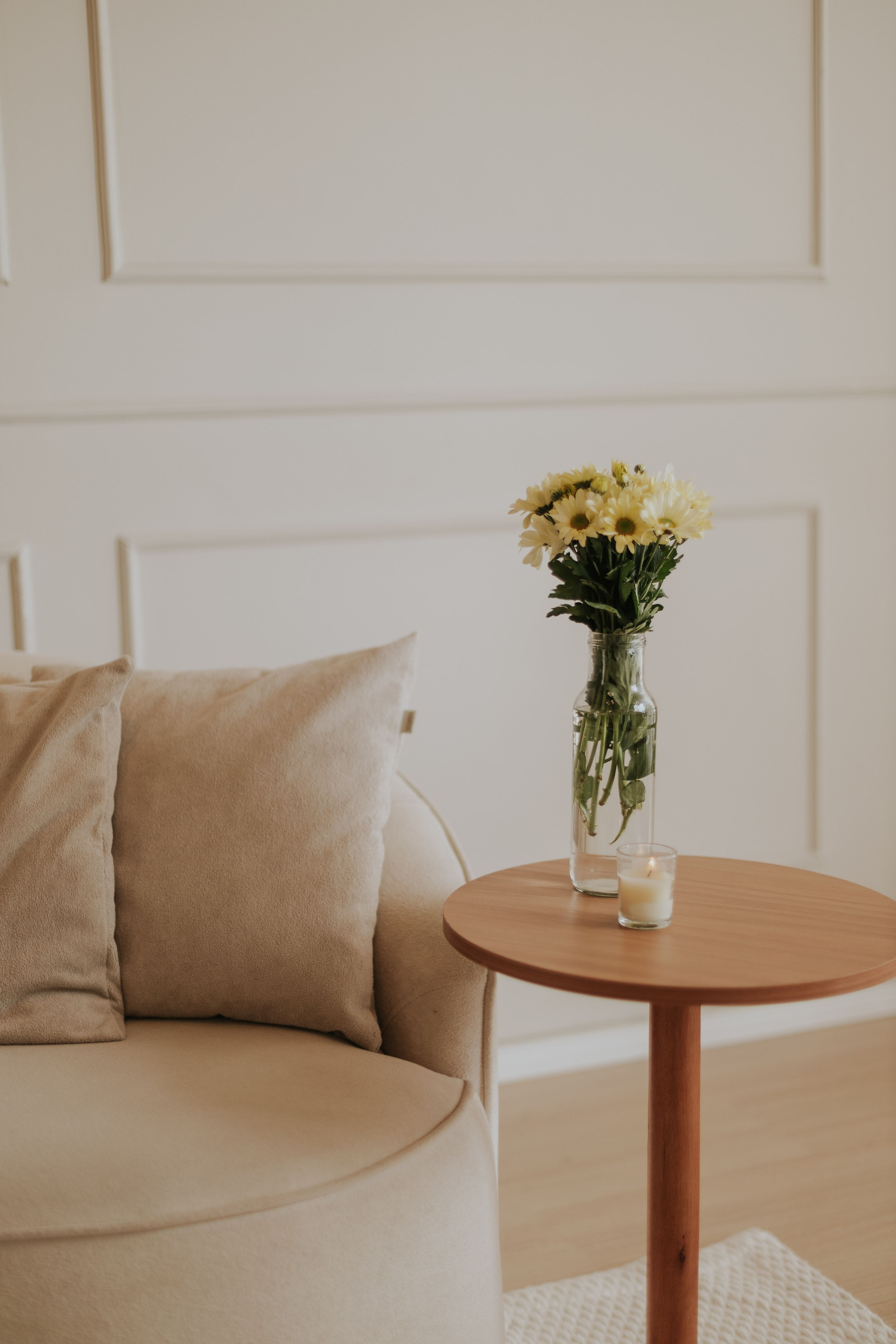 Interior sereno de sala de estar minimalista com uma aconchegante poltrona bege e um vaso de flores amarelas.