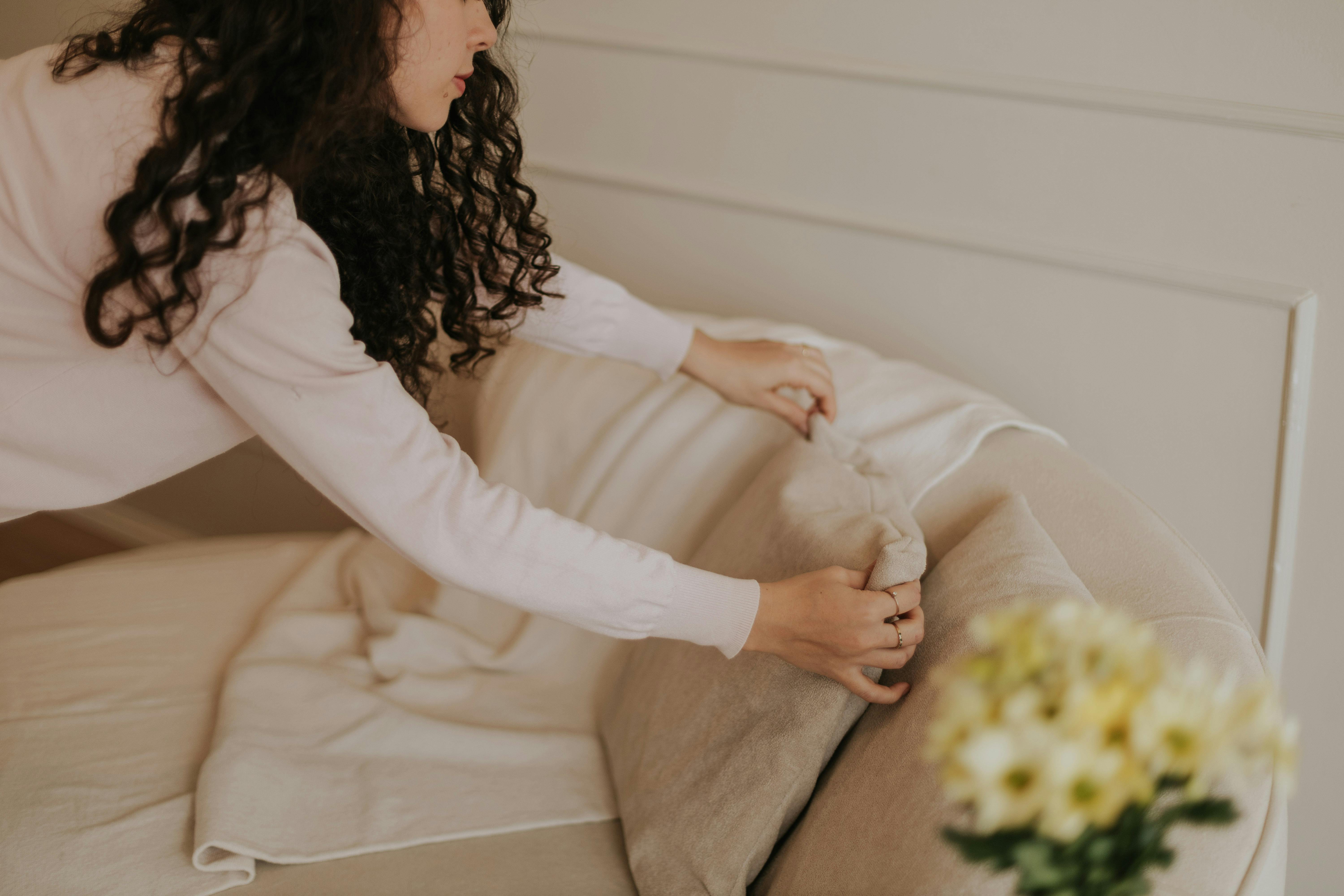 A woman arranging cushions in a cozy, minimalist living room.