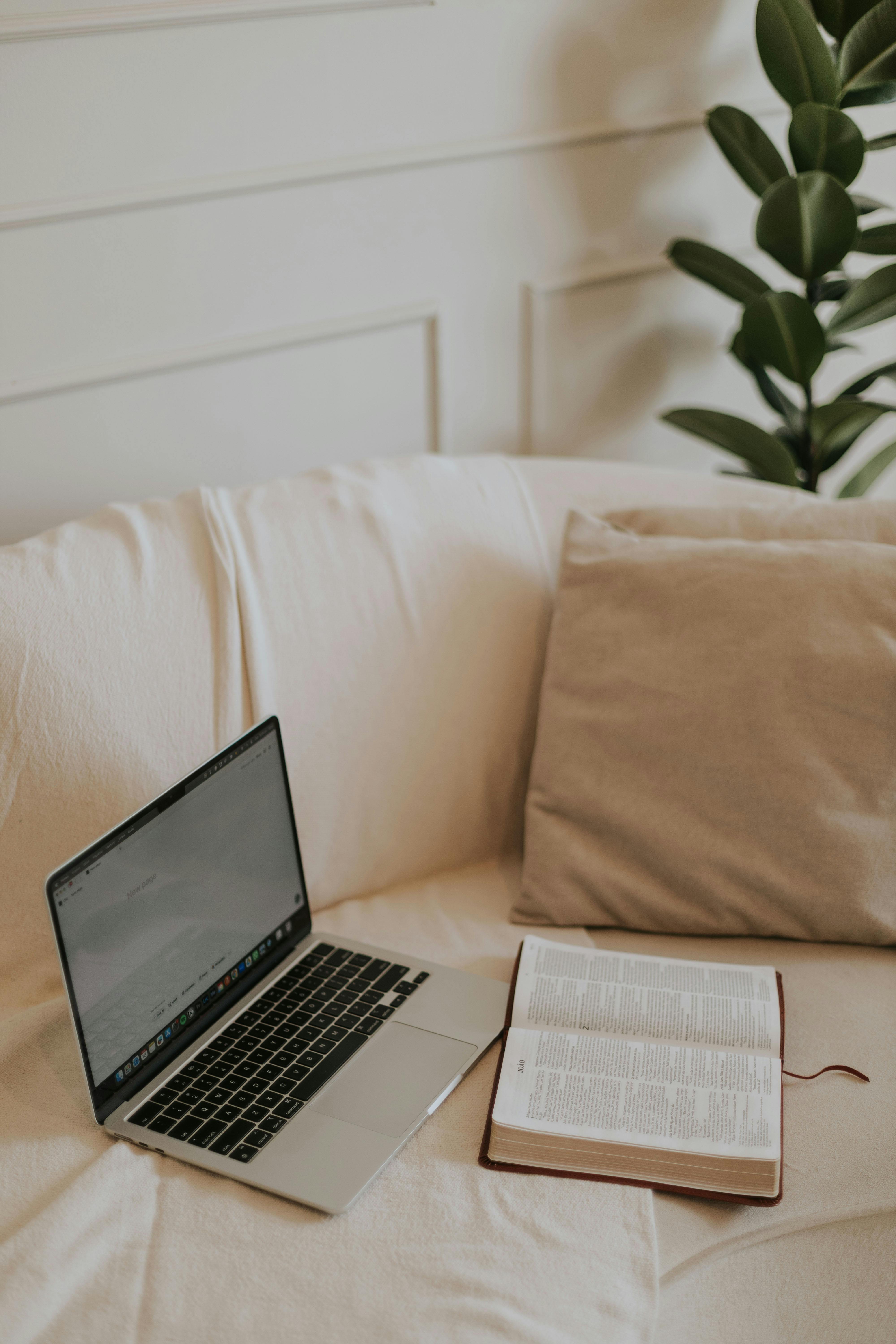Cozy indoor setup with an open Bible and laptop on a sofa, perfect for a devotional moment.