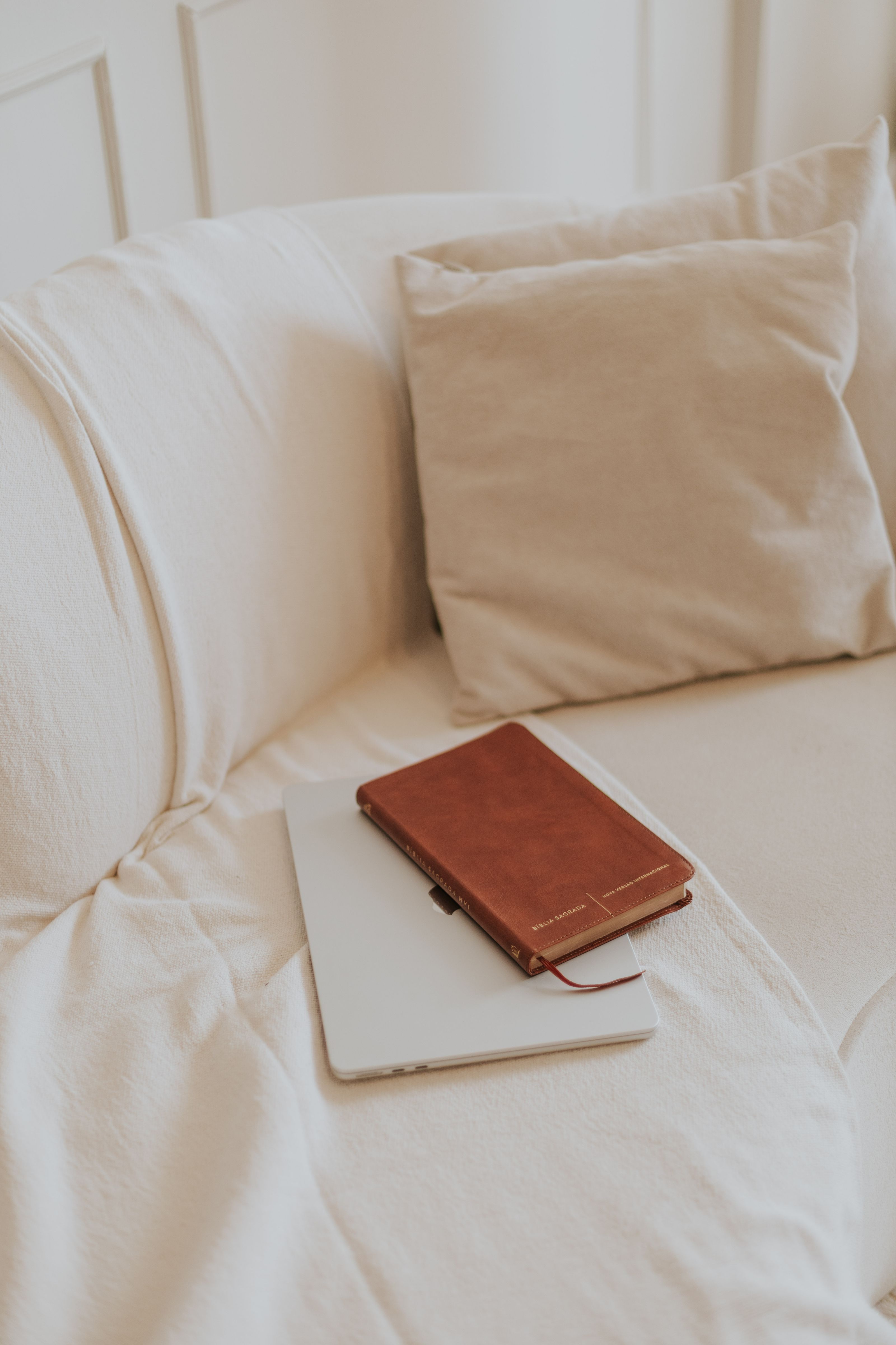 Um caderno de couro e um tablet ficam sobre um sofá bege macio, criando um recanto de leitura calmo e convidativo.