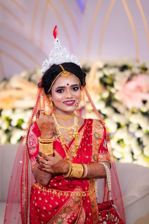 Free Bengali bride in red saree with traditional jewelry and headpiece, smiling indoors. Stock Photo