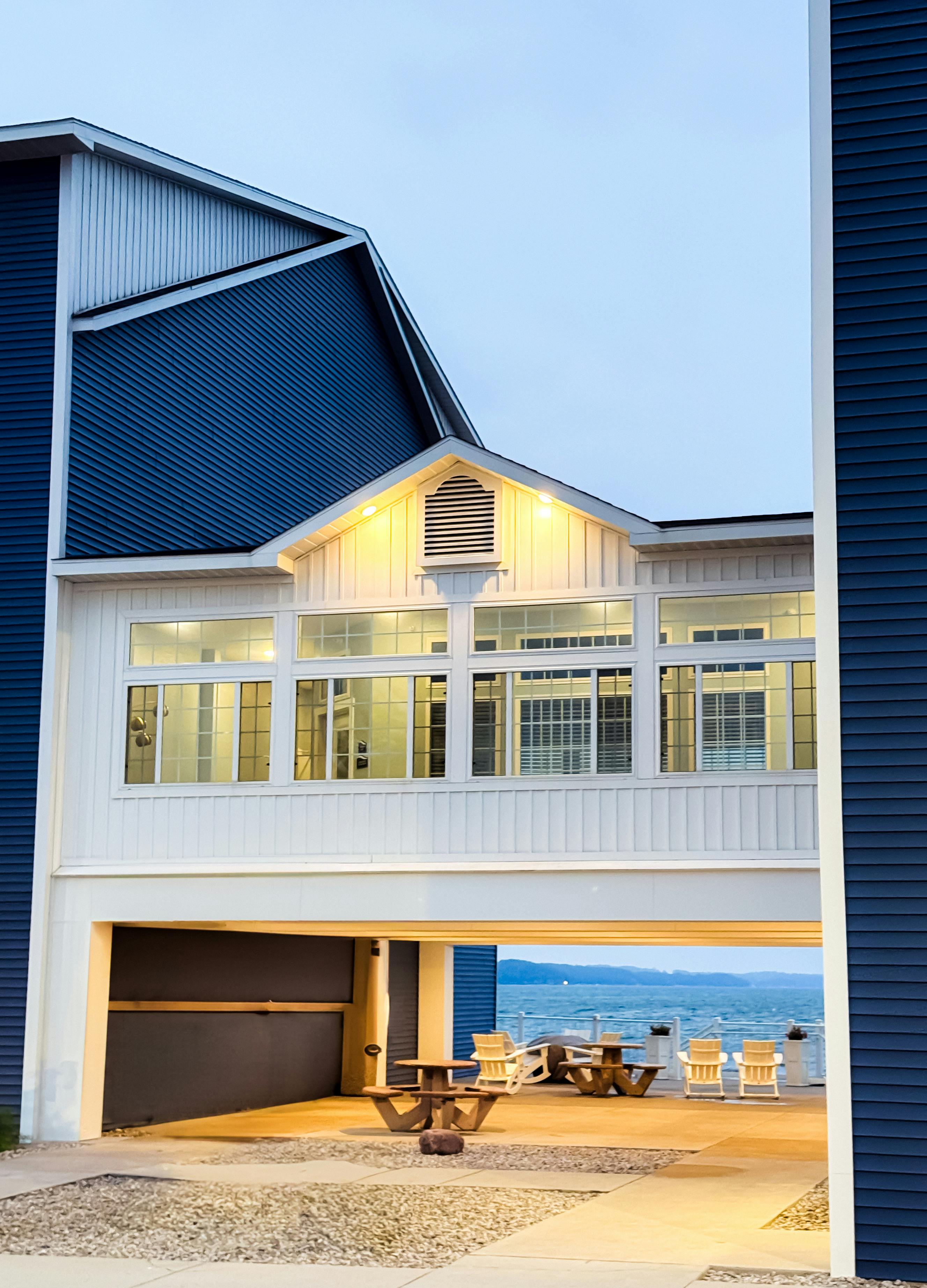 Modern building with patio area and ocean view at twilight, featuring wooden chairs.