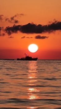 A breathtaking sunset scene with a silhouetted boat on calm waters, evoking tranquility.