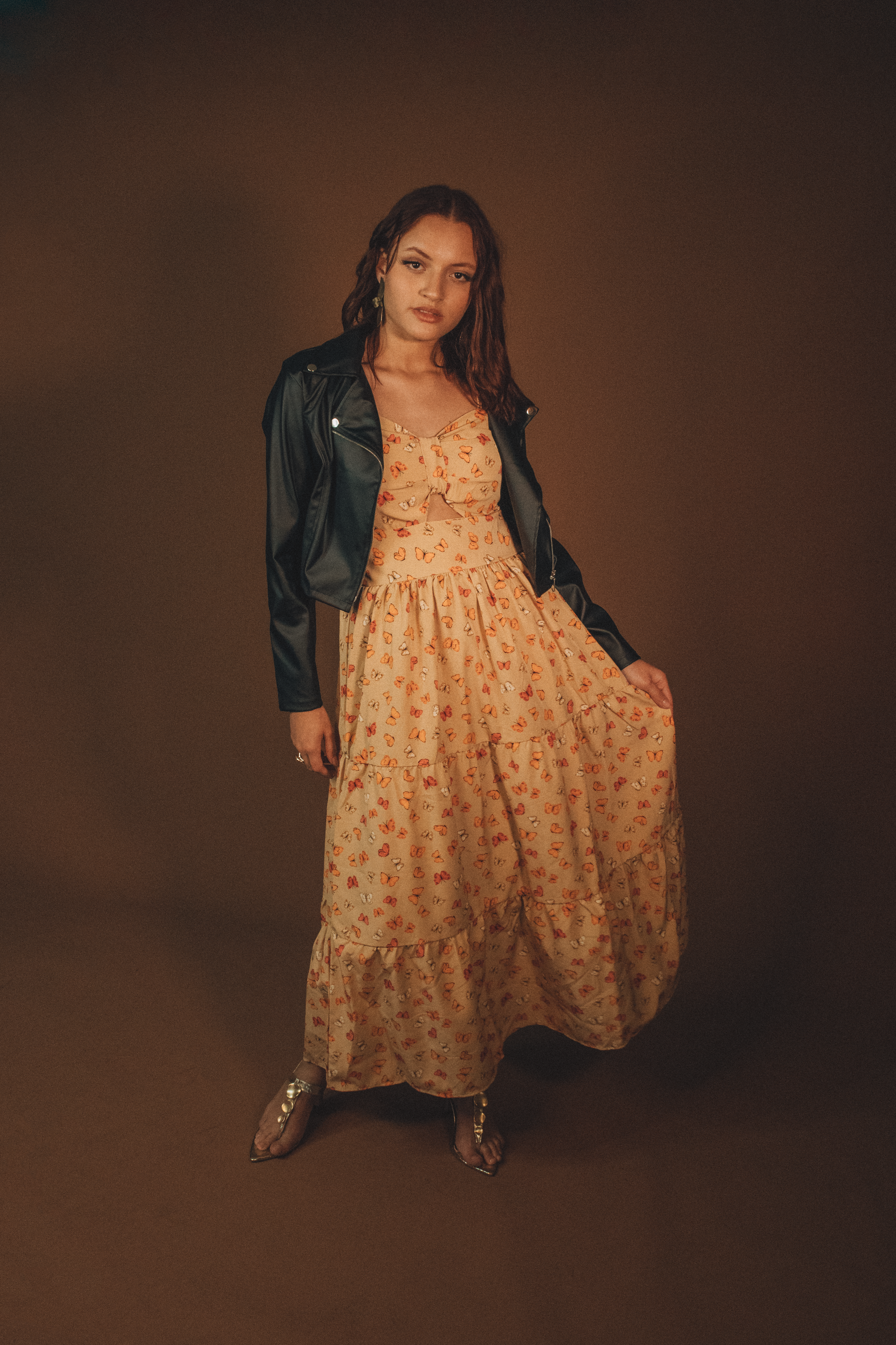 Stylish woman posing in floral dress and leather jacket against a neutral backdrop.