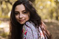 A woman smiling in a natural setting with sunlight and bokeh effect.