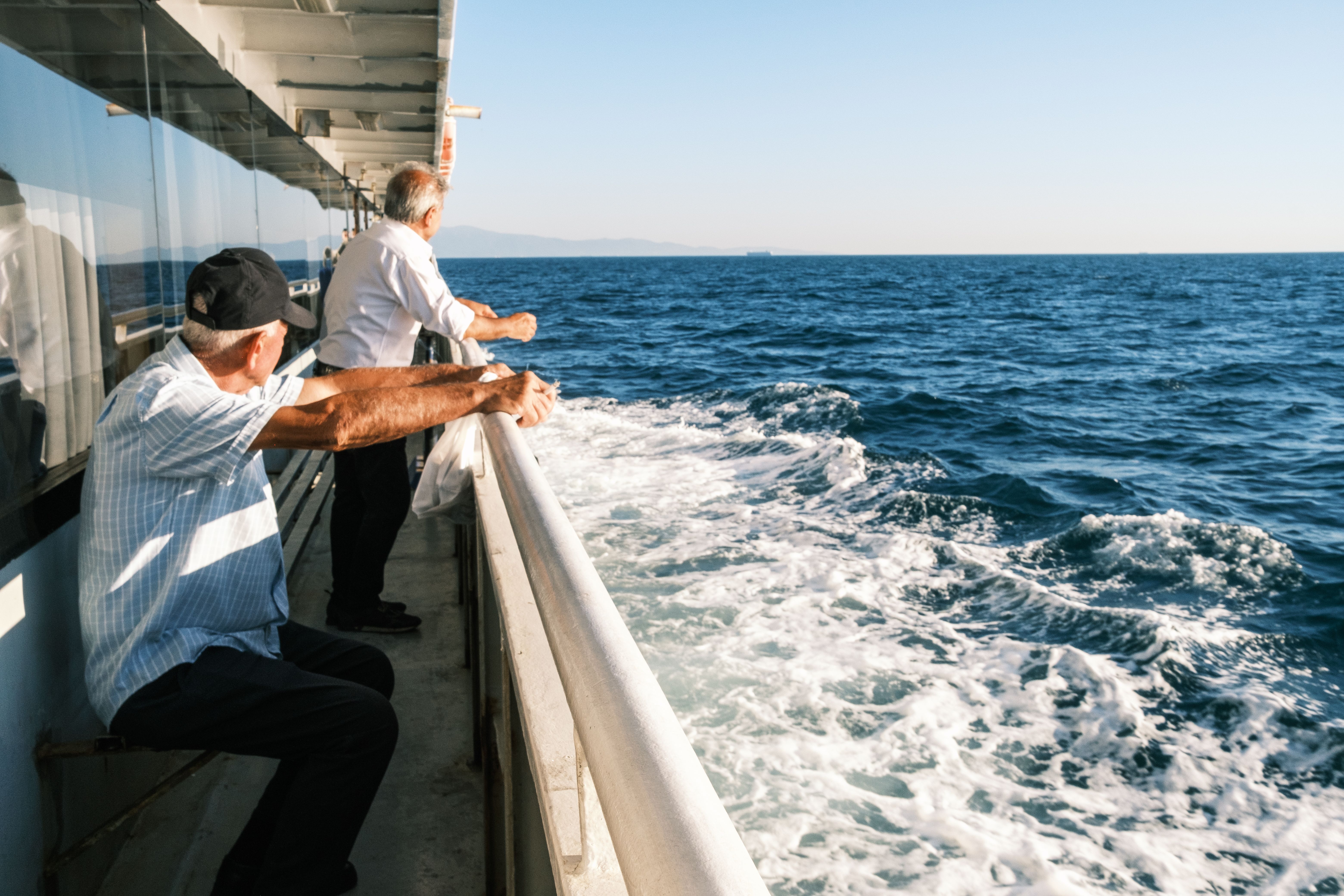Two senior men enjoy the ocean view from a ferry deck on a sunny day.