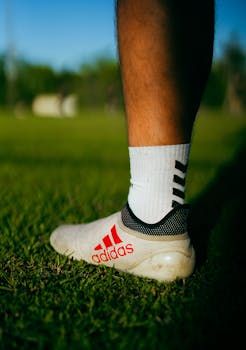 Side view of an Adidas soccer shoe on a sunny grass field.