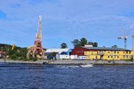 A scenic waterfront in Stockholm featuring a colorful industrial setup with a boat sailing by on a sunny day.