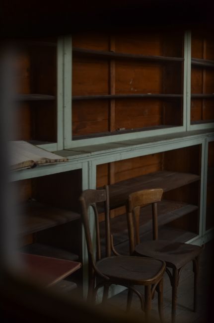 Moody interior view of an abandoned room featuring vintage wooden chairs and empty shelves.