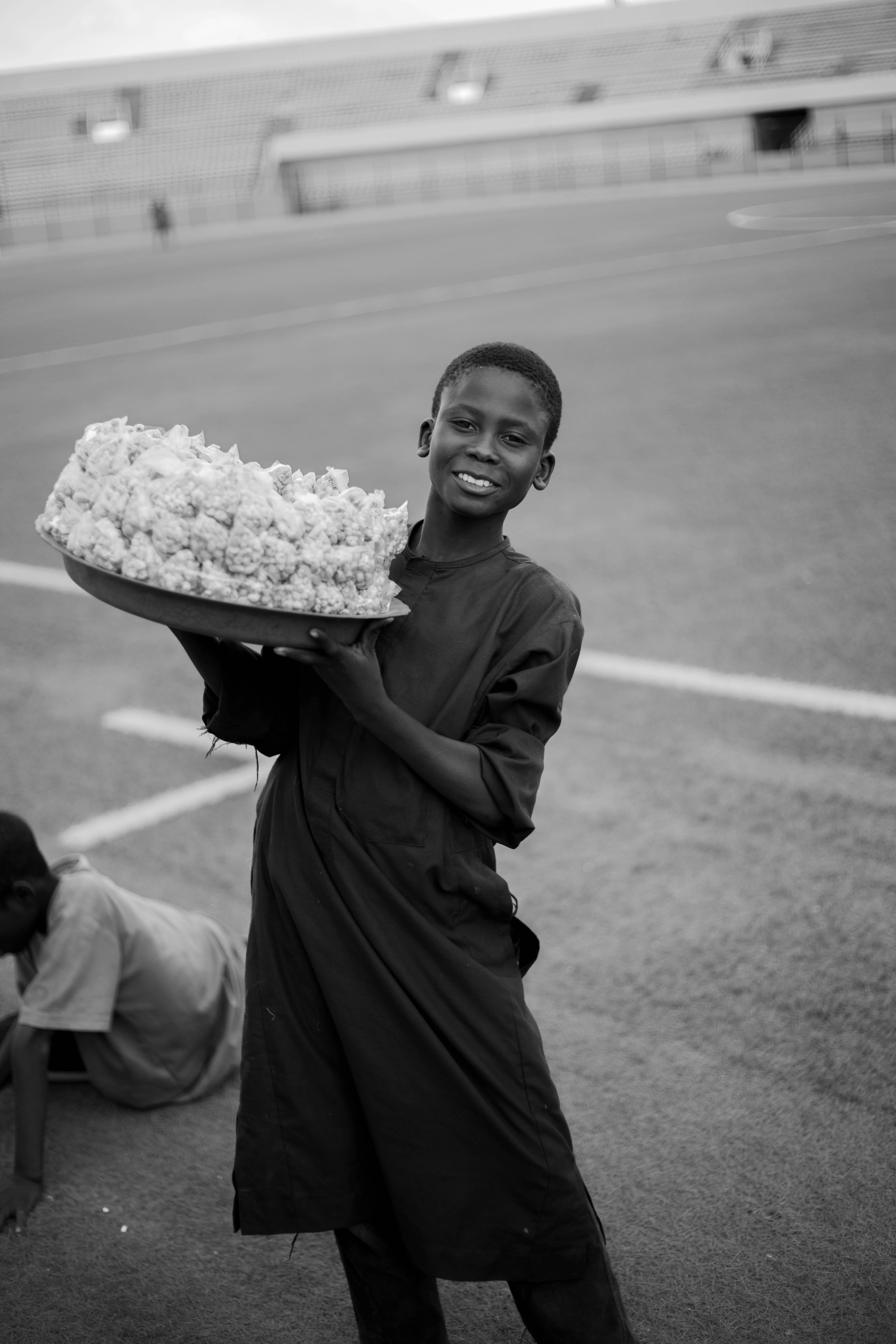 Gratuit Un jeune vendeur de pop-corn souriant tout en tenant un plateau dans un stade en plein air Photos