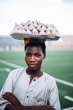 Portrait of a young vendor balancing snacks on a tray outdoors, showcasing cultural resilience.