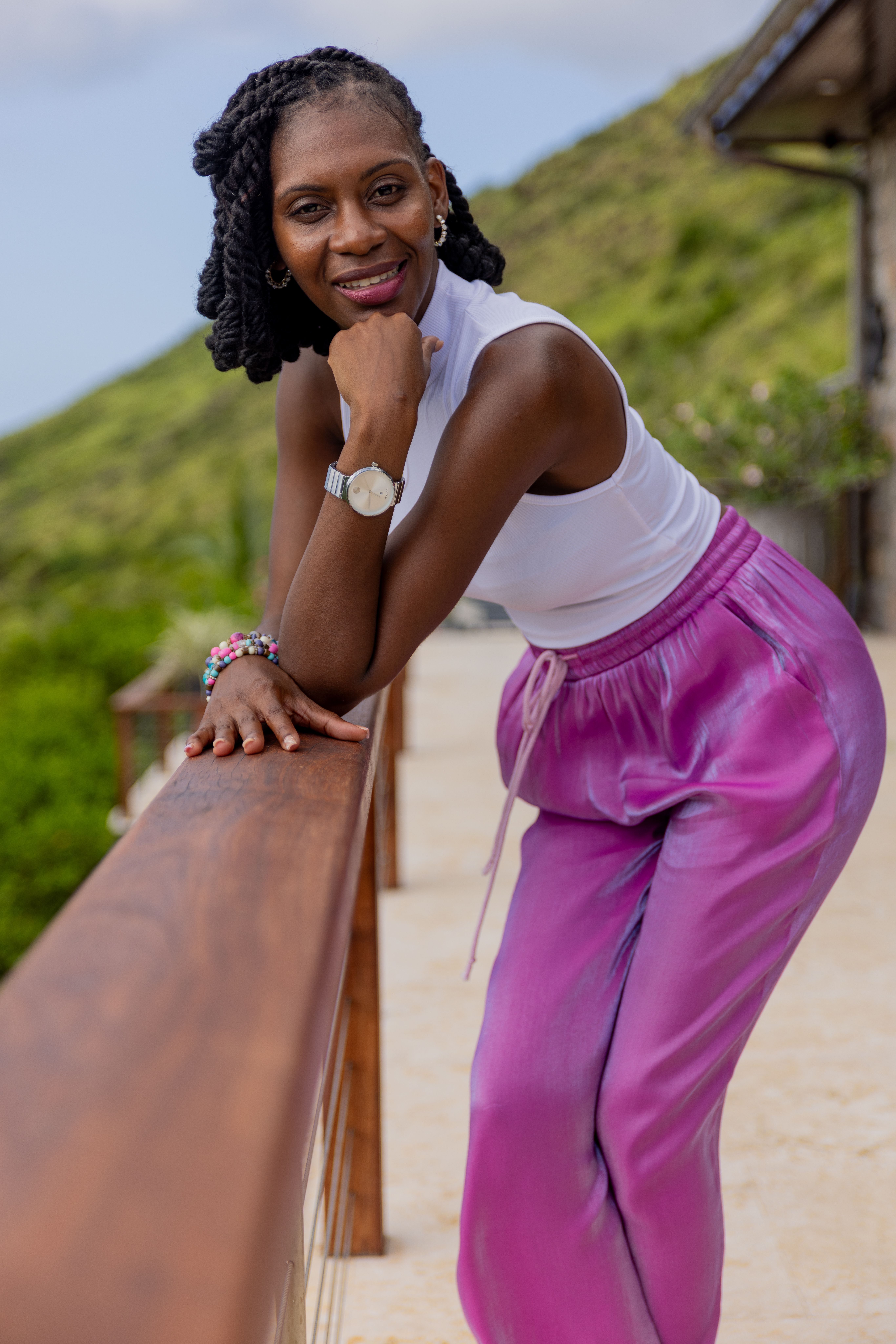 A woman in vibrant attire leans on a railing enjoying a sunny day outdoors, evoking a sense of joy and relaxation.
