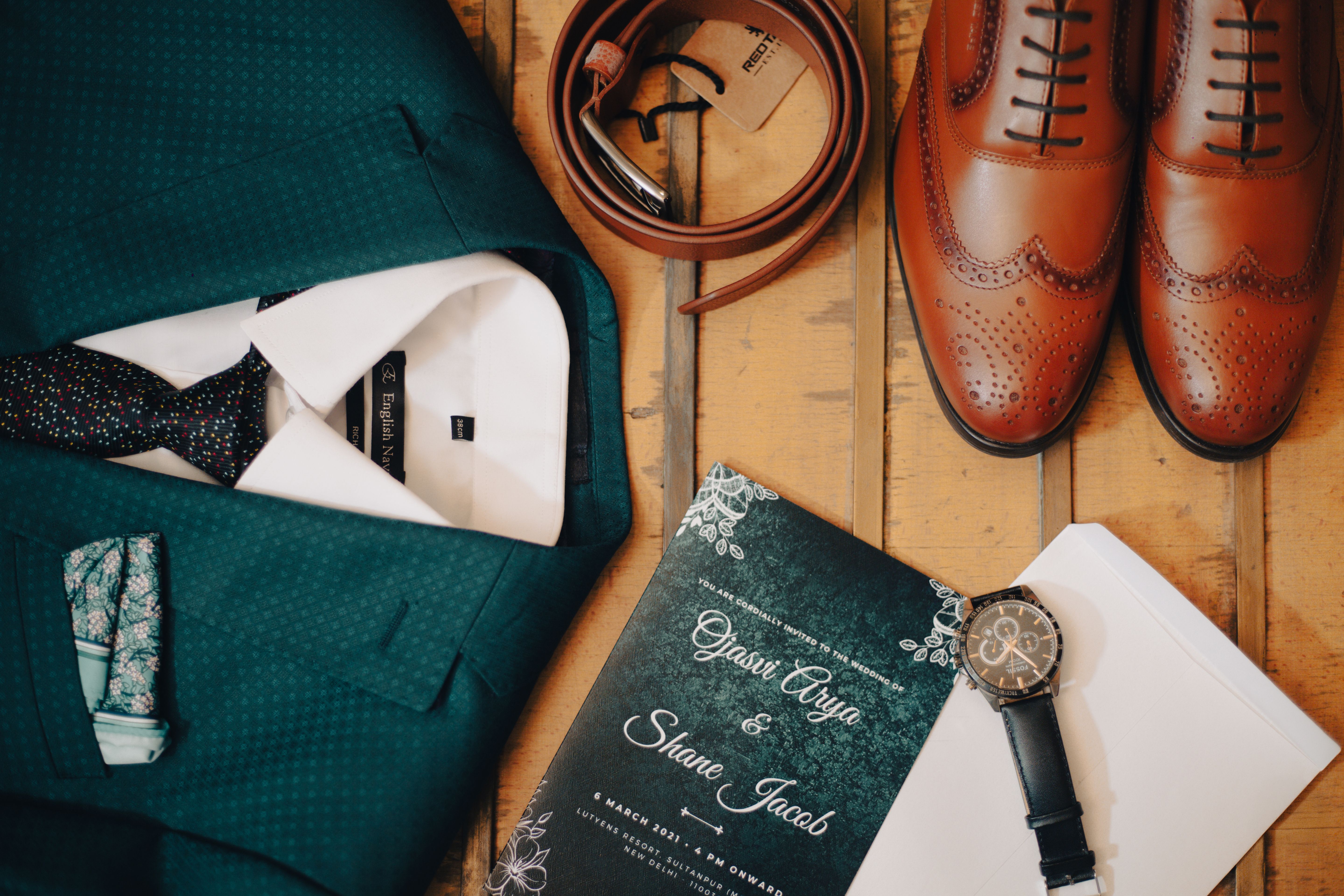 Classic men's wedding accessories flat lay featuring suit, shoes, and invitation.