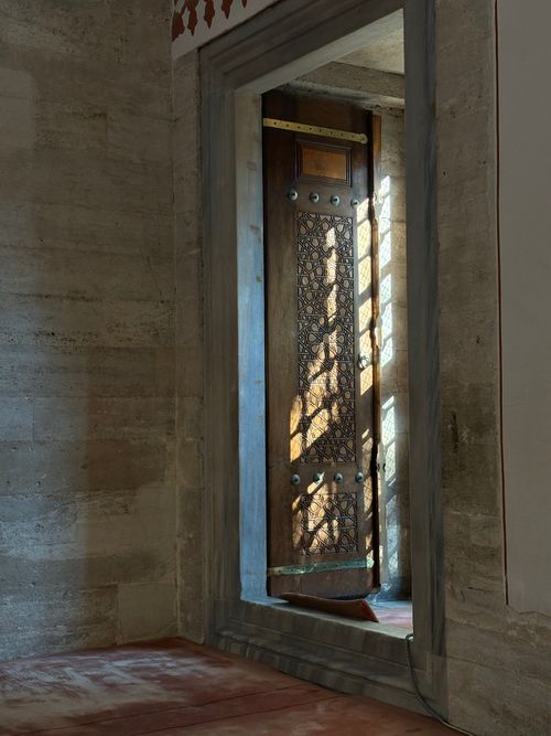 Free Beautiful sunlight casts patterns through a wooden door in a historic stone structure. Stock Photo