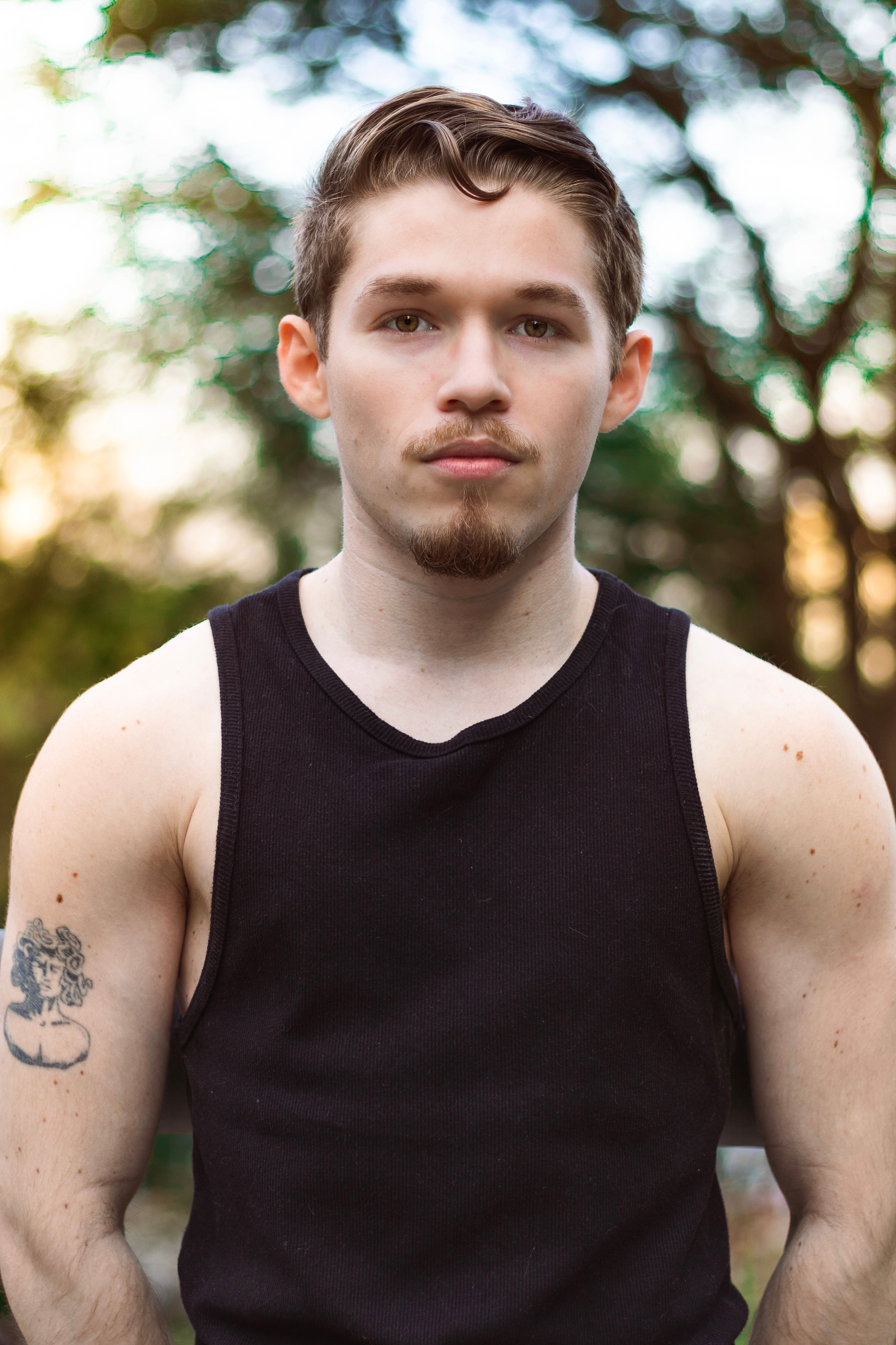 Portrait of a young man with a confident look in a black tank top outdoors. Natural background.