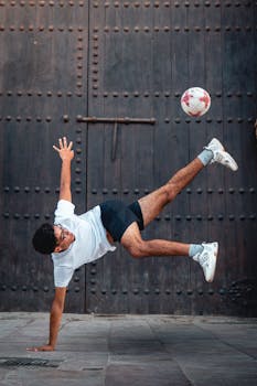 Young man performing an acrobatic soccer trick in front of a rustic urban backdrop.