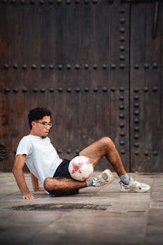 A young male athlete skillfully balancing a soccer ball on foot against a rustic wooden backdrop.