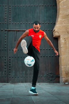 Adult male performing freestyle soccer tricks in an outdoor urban environment.