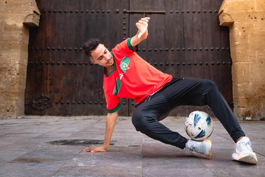 A young man skillfully performs a soccer trick with a ball, showcasing talent and athleticism in a vibrant urban setting.