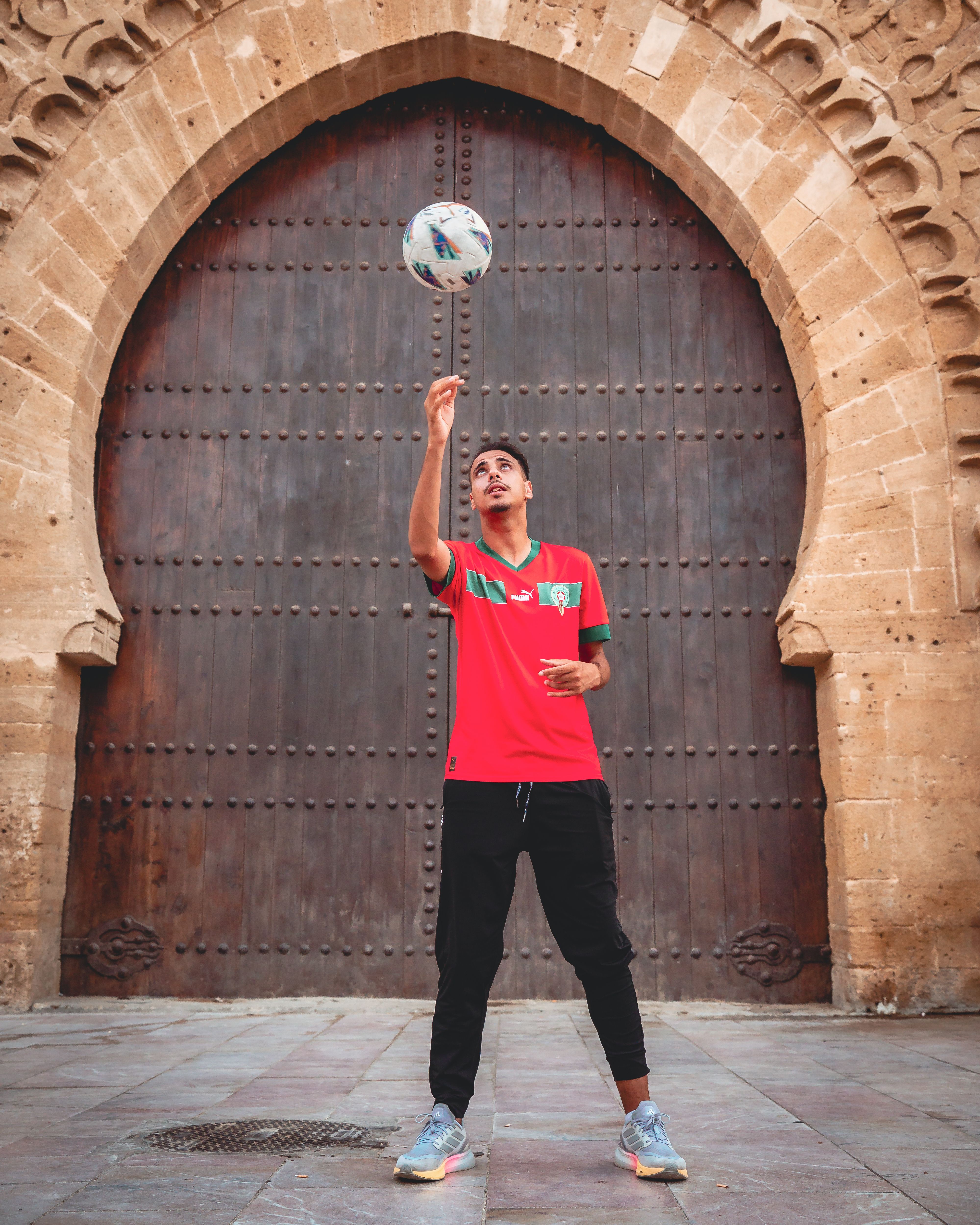 Young man skillfully bouncing a soccer ball in front of a historic stone archway. Perfect for sports and culture themes.