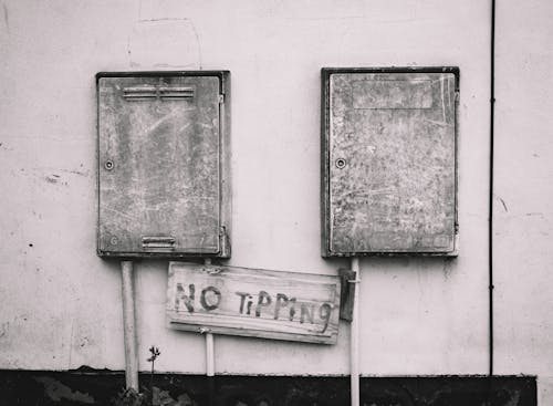 Free Black and white image of rusty electrical boxes with 'No Tipping' sign adds urban decay aesthetic. Stock Photo
