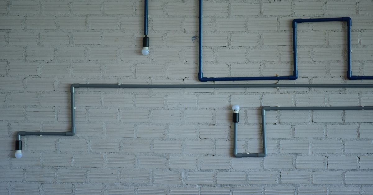 Industrial style light fixture with pipes and bulbs on a white brick wall. Modern design element.
