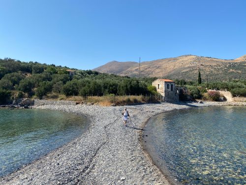Free A person walking along a rocky beach with scenic Greek countryside views and historic architecture. Stock Photo