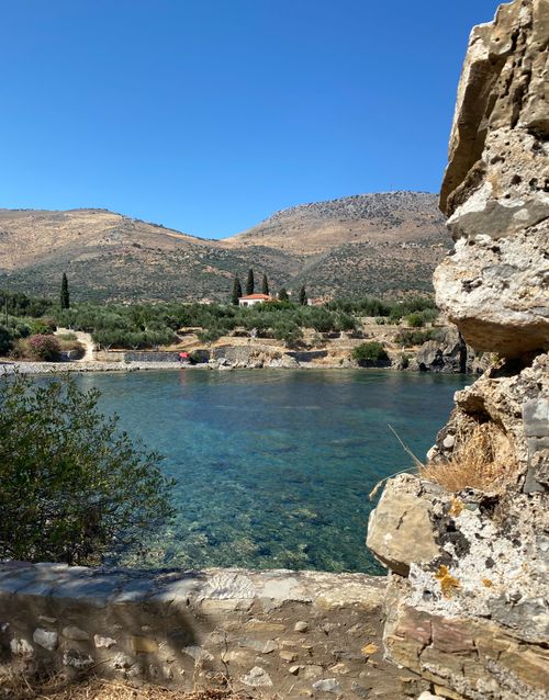 Free Tranquil view of Gerolimenas harbor with clear blue water and mountainous backdrop. Stock Photo