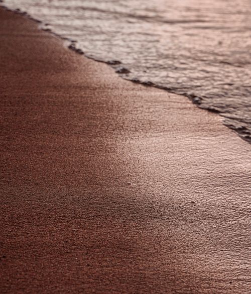 Free Serene view of the sandy shoreline gently kissed by ocean waves at sunrise. Stock Photo