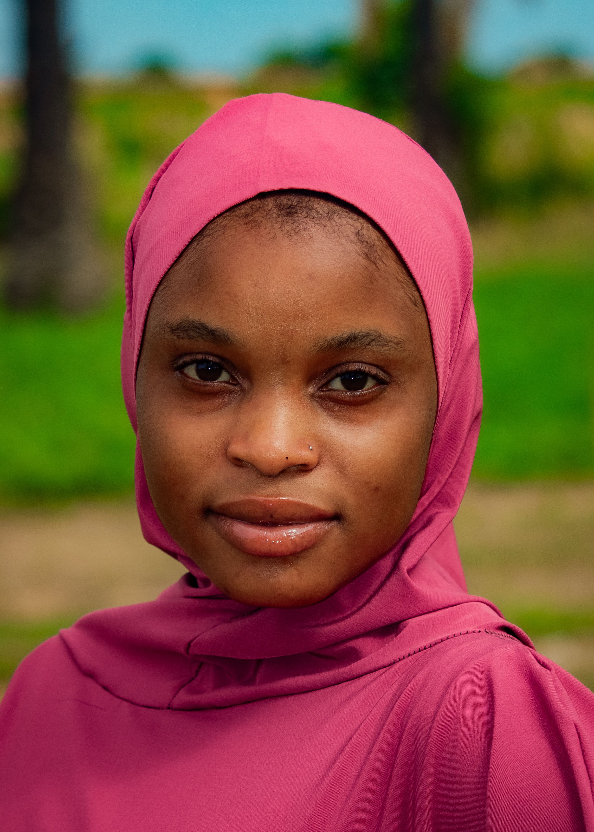 Close-up portrait of a woman wearing a pink hijab with a serene expression outdoors.