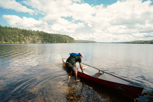 A man prepares his canoe for a lake adventure under a clear blue sky in Cloyne, Ontario.
